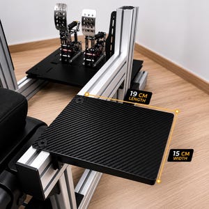 May include: A black carbon fiber textured side tray mounted on a silver aluminum racing simulator rig. The tray measures 19 cm in length and 15 cm in width. The text BALTIC MOTORSPORT SOLUTIONS is visible at the top of the frame.