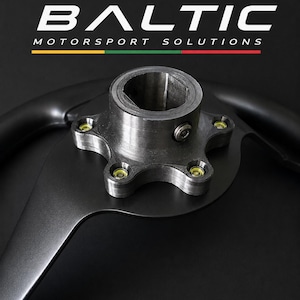 May include: A black steering wheel hub adapter featuring a central cylindrical mount with a splined interior and five bolt holes. The text BALTIC MOTORSPORT SOLUTIONS is printed above the hub with a horizontal yellow, green, and red line.