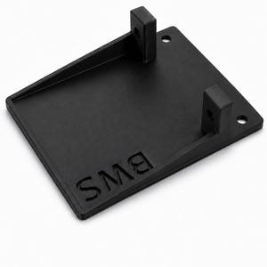 May include: A black, rectangular, flat mounting bracket featuring two vertical tabs with circular holes, two additional circular holes on the base, and the embossed text "BMS" on the surface. The logo "BALTIC MOTORSPORT SOLUTIONS" appears below.