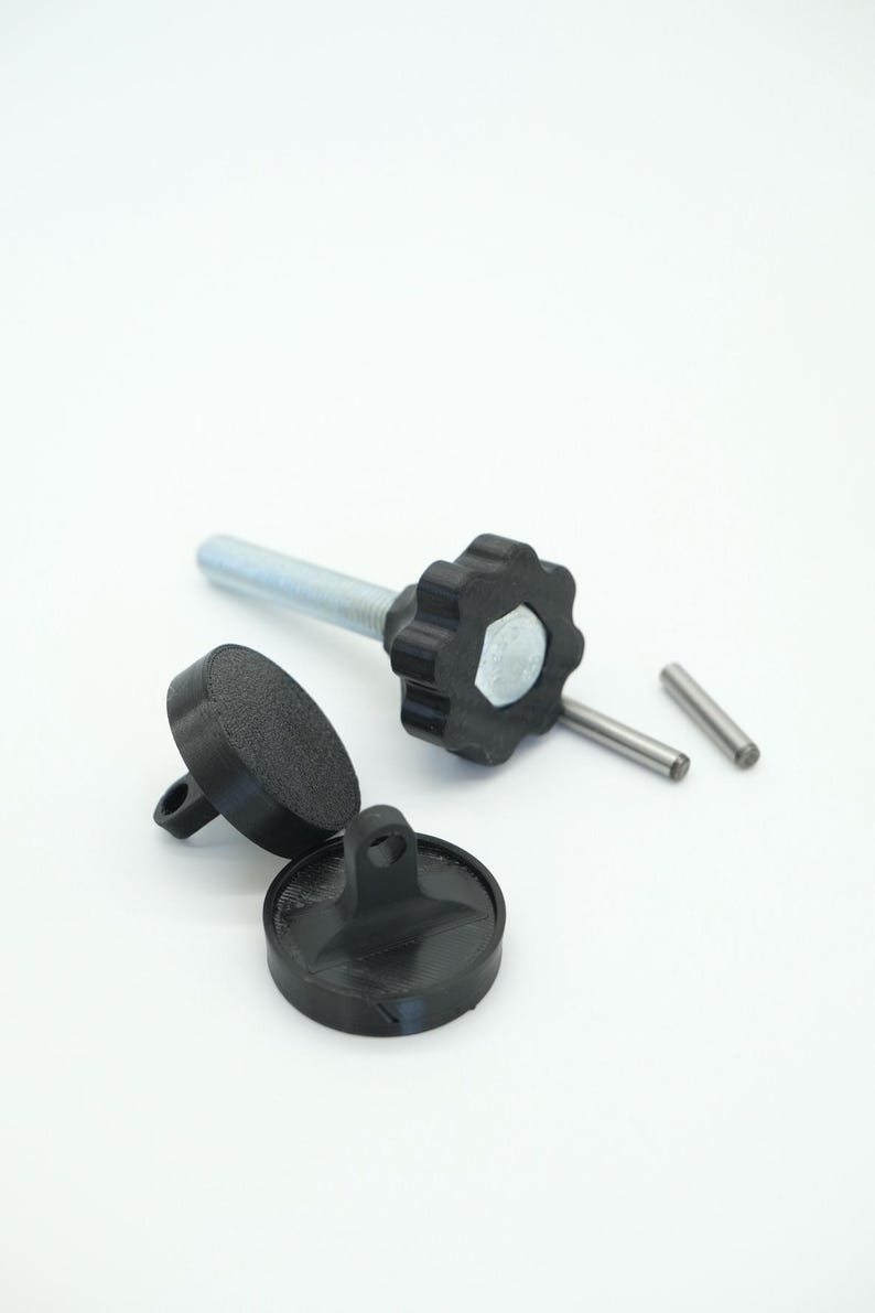 Pu&ograve; includere: Una collezione di componenti hardware neri, tra cui un bullone filettato con una manopola a forma di stella, due piccoli perni cilindrici e due pezzi circolari con un anello. I componenti sono su sfondo bianco.