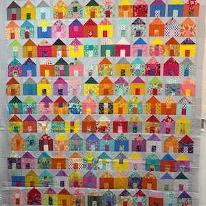 May include: A colorful quilt featuring a repeating pattern of small houses. Each house is a different color and pattern, including pink, yellow, blue, and orange. The quilt has a gray background.