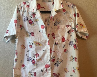 May include: White button-up shirt with a pattern of gardening tools, hats, flowers, and price tags in red, yellow, and purple. The short-sleeved shirt is hanging on a black hanger.