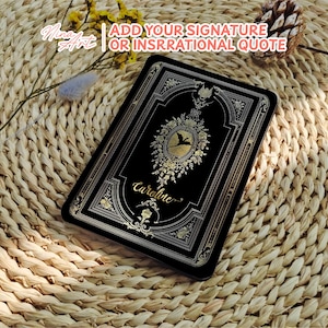 May include: A black book cover with gold accents and a floral design. The book cover has the name "Caroline" written in gold script.