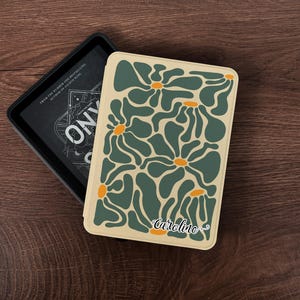 May include: A deck of cards with a floral design in shades of green and orange on a cream background. The name "Caroline" is printed on the bottom. The deck is next to a black box with the text "ONYX". The top left corner has the text "NINA ART".