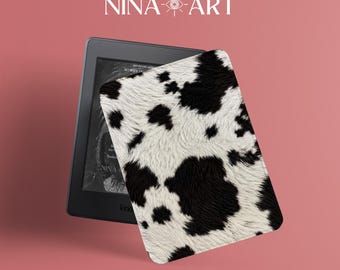 May include: A black e-reader device featuring a protective cover with a black and white cow print pattern. The screen displays a book cover with text, and the brand name NINA-ART is visible at the top of the image against a solid pink background.