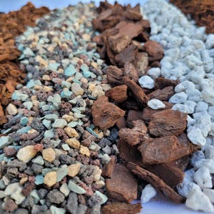 May include: A collection of potting soil components arranged in vertical rows, including black charcoal, brown wood bark chips, multicoloured volcanic rock, larger brown bark chunks, white perlite, and dark brown fibrous coconut coir.