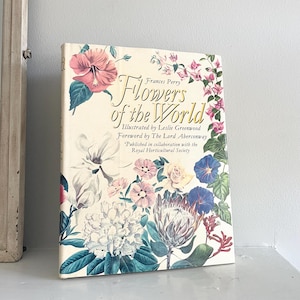 May include: A hardcover book titled "Flowers of the World" with floral illustrations. The cover features a variety of colorful flowers, including hibiscus, magnolia, and protea, with the title in elegant script. The book is published in collaboration with the Royal Horticultural Society.