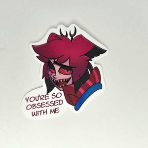 May include: A sticker featuring a cartoon character with red hair, black accents, and a sinister grin. The character is wearing a red and black striped outfit. Text on the sticker reads "YOU'RE SO OBSESSED WITH ME."