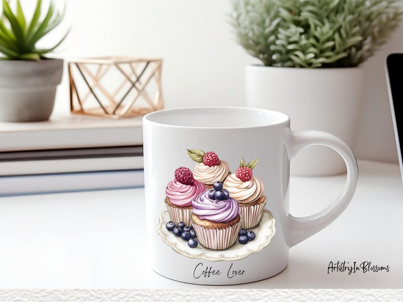 May include: White ceramic coffee mug with a design of four cupcakes with pink, purple, and white frosting topped with raspberries and blueberries. The mug has the text "Coffee Lover" printed on the bottom.