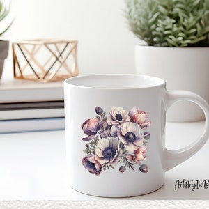 Pu&ograve; includere: Tazza in ceramica bianca con un design floreale che presenta un bouquet di anemoni viola, rosa e bianchi. La tazza ha un manico nero e il testo "Artistry In Blossoms" &egrave; stampato sul fondo.