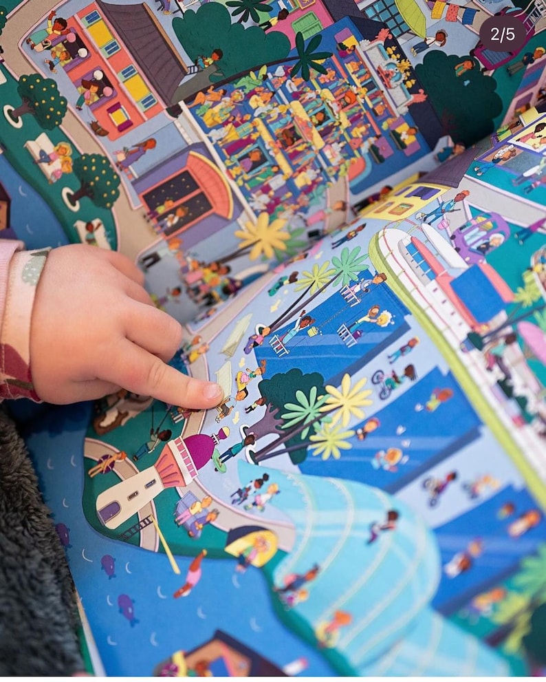 May include: A colorful children's book with a busy city scene on one page and a beach scene on the other. The book is open and a child's hand is pointing at the beach scene.