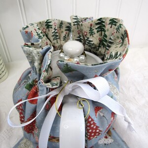 May include: A blue teapot cozy with a white ribbon and a Christmas tree print. The cozy is lined with a beige fabric with a green Christmas tree print.