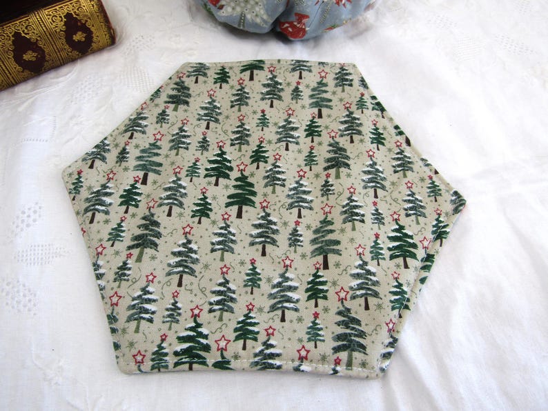 May include: A hexagonal beige placemat with a repeating pattern of green Christmas trees and red stars.