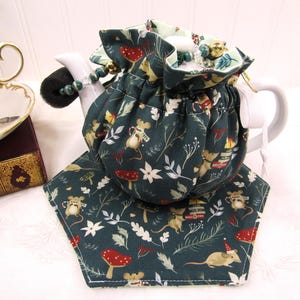 May include: A green teapot cozy with a white drawstring and a pattern of mice and mushrooms. The cozy is on a hexagonal green and white coaster with a similar pattern.