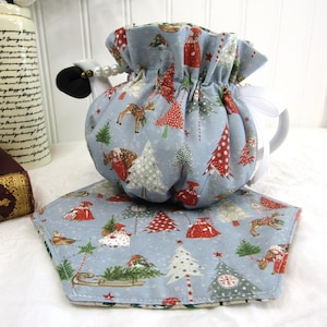 May include: A blue teapot cozy with a Christmas tree and reindeer print. The cozy has a white drawstring and is sitting on a matching blue and white Christmas tree print placemat.