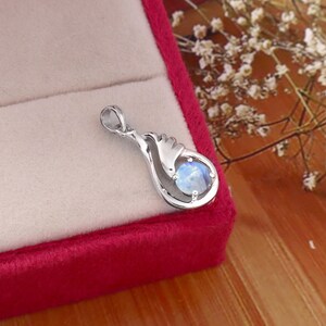 May include: A silver-toned pendant featuring a smooth, round, iridescent moonstone set within a curved, teardrop-shaped metal frame. The pendant includes a small circular bail at the top for attachment to a chain, showcasing a polished finish.
