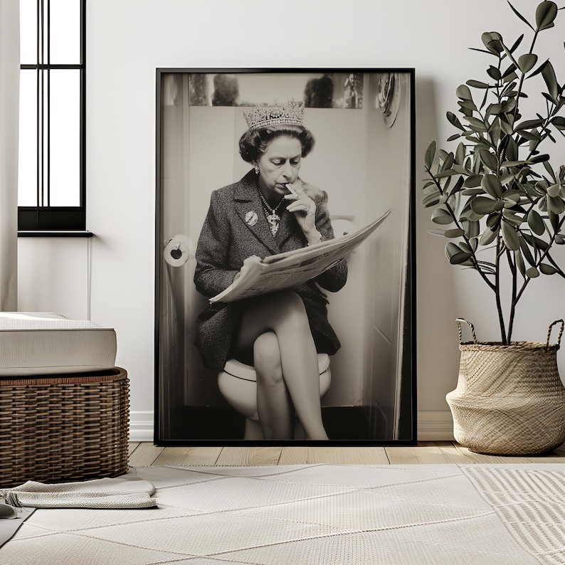 May include: Black and white framed print of a person wearing a crown and blazer, seated on a toilet while reading a newspaper. The image is in a bathroom setting, with a roll of toilet paper visible. A plant in a woven basket is in the background.