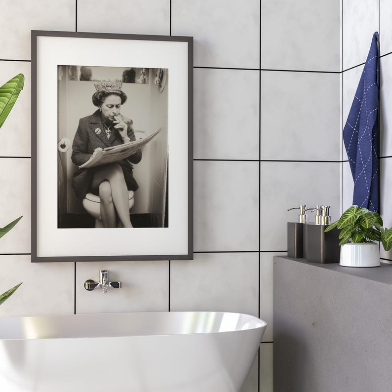 May include: Framed black and white print of a person wearing a crown, smoking a cigarette, and reading a newspaper while seated on a toilet. The print is in a bathroom setting with a white tub.