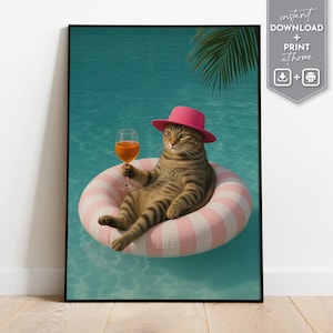 May include: A framed print featuring a tabby cat wearing a pink hat and floating in a pool on a pink and white striped inflatable ring. The cat holds a glass of orange liquid. Palm fronds are visible in the background. The words "instant download + print at home" are in the upper right corner.