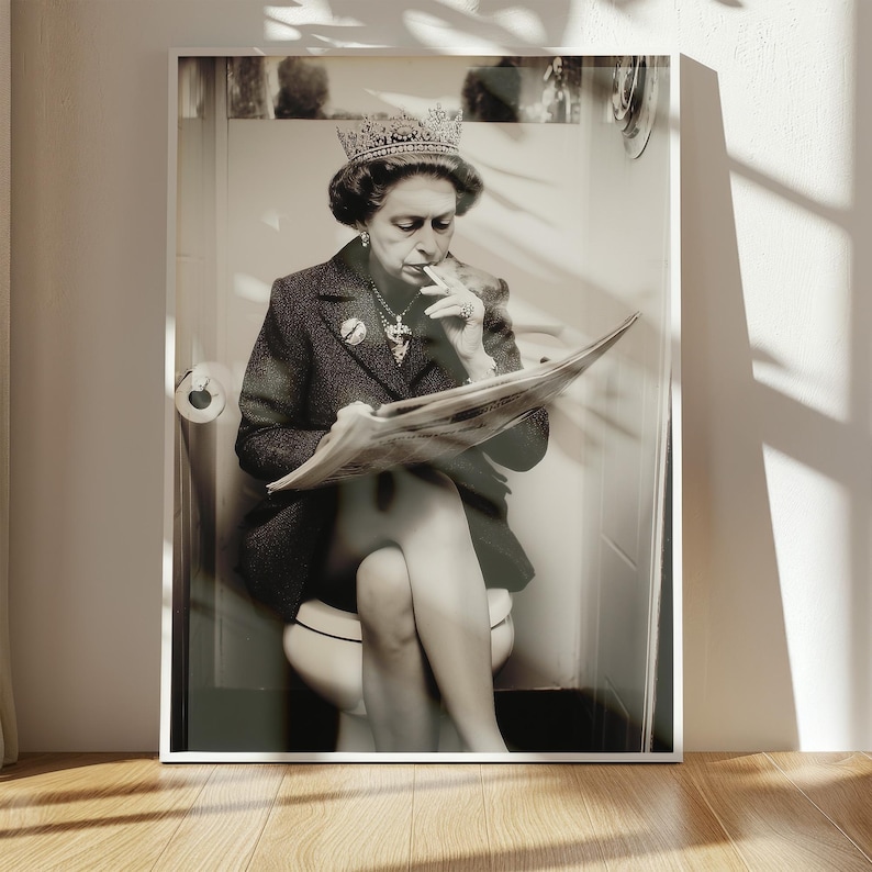 May include: Black and white framed print of a person wearing a crown, jewelry, and a blazer, sitting on a toilet, smoking a cigarette, and reading a newspaper. The print is in a white frame.