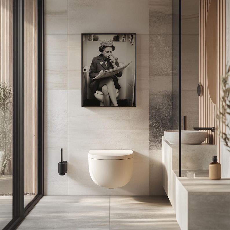 May include: A modern bathroom featuring a wall-mounted toilet with a soft, curved design. A framed black and white photograph hangs above the toilet. The bathroom has a minimalist aesthetic with neutral tones and a large window.
