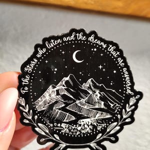 May include: Black and white sticker with a mountain range, crescent moon, and stars. The text reads "To the stars who listen and the dreams that are answered".