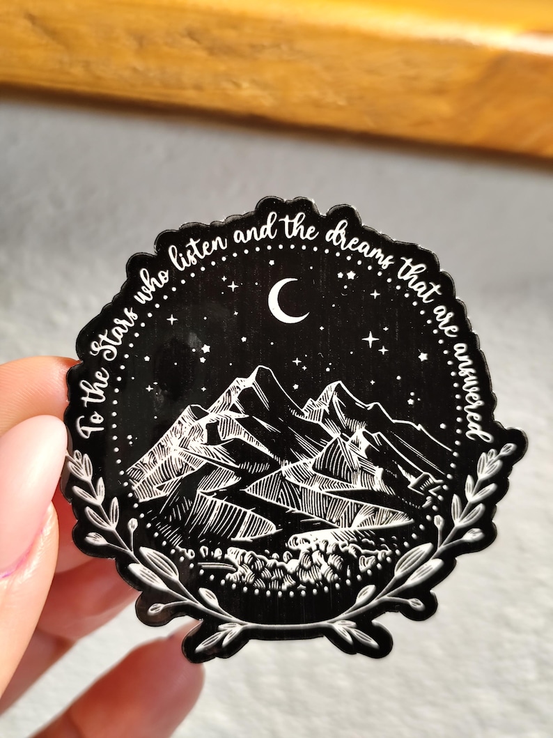 May include: Black and white sticker with a mountain range, crescent moon, and stars. The text reads "To the stars who listen and the dreams that are answered".
