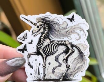 May include: A black and white sticker of a skeletal unicorn with a flowing mane and tail. The unicorn is standing in a field of grass with butterflies flying around it.
