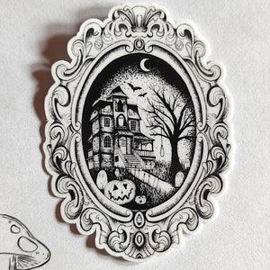 Puede incluir: Ilustración en blanco y negro de una casa encantada con una luna creciente, murciélagos y una soga para ahorcar en un marco ovalado decorativo.