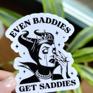Op de afbeelding: Een witte sticker met een zwart-wit illustratie van een huilende koningin met een kroon en een parelketting. De sticker heeft de tekst "EVEN BADDIES GET SADDIES" in het zwart.