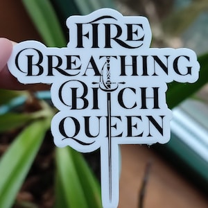 Könnte beinhalten: Weißer Aufkleber mit schwarzem Text, der "Fire Breathing Bitch Queen" lautet, mit einem Schwertmuster in der Mitte.