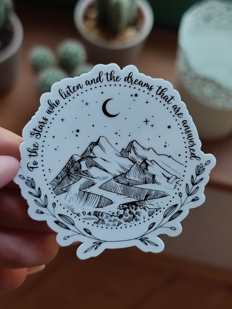 May include: A white sticker with a black and white illustration of mountains, a crescent moon, and stars. The text around the image reads "To the stars who listen and the dreams that are answered."