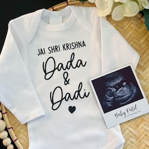 Peut inclure: Combinaison bébé à manches longues blanche avec un texte noir qui dit "Jai Shri Krishna Dada & Dadi" avec un petit cœur noir. Une image d'échographie en noir et blanc est sur la combinaison avec le texte "Baby Patel due September 2023".
