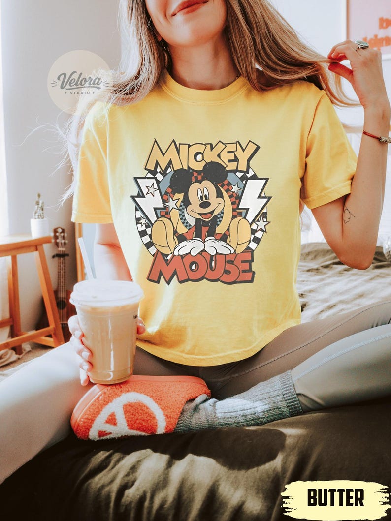 Puede incluir: Camiseta amarilla con un gr&aacute;fico de Mickey Mouse y el texto "Mickey Mouse". El dise&ntilde;o tiene un estilo retro con estrellas, rayos y un patr&oacute;n de cuadros. La camiseta est&aacute; hecha de un material suave y c&oacute;modo.