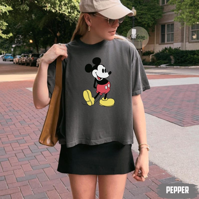 May include: A dark gray t-shirt featuring a classic Mickey Mouse graphic. The cartoon character is depicted in his iconic red shorts, yellow shoes, and white gloves. The word "PEPPER" is printed in white at the bottom right.