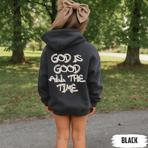 May include: A black hooded sweatshirt with the text "GOD IS GOOD ALL THE TIME" in a white, stylized font. The sweatshirt is worn by a person with a large tan bow in their hair. The word "BLACK" is in a white box at the bottom.