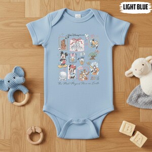 Puede incluir: Body de beb&eacute; azul claro con un dise&ntilde;o colorido de Disney World. El dise&ntilde;o incluye a Mickey y Minnie Mouse, el Pato Donald, Chip y Chop, y el texto "Walt Disney World" y "2026".