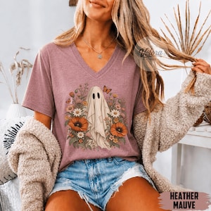 May include: A heather mauve V-neck t-shirt featuring a graphic print of a white ghost surrounded by colourful flowers and butterflies. The shirt is paired with blue denim shorts and a beige textured cardigan, with the text Heather Mauve visible.