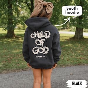Pode incluir: Moletom preto juvenil com a frase "CHILD OF GOD" e "PSALM 23" em branco, com estilo grafite. O moletom tem capuz com cordão e bolso canguru. A palavra "BLACK" está na parte inferior da imagem.