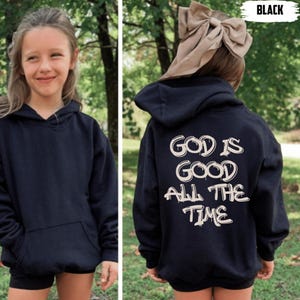 May include: Black hoodie with the text "GOD IS GOOD ALL THE TIME" in white. The hoodie has a front pocket and a hood. The image shows a young person wearing the hoodie. The word "BLACK" is in the top right corner.