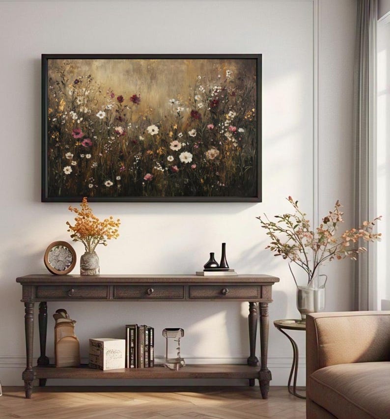 Puede incluir: Una consola de madera marr&oacute;n con tres cajones y un estante inferior. La mesa tiene patas torneadas y est&aacute; decorada con una pintura de un campo de flores silvestres en un marco marr&oacute;n oscuro.