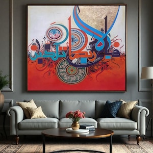 May include: Large framed artwork featuring Arabic calligraphy in vibrant colors. The artwork has a red and white background with blue, orange, and gold accents. The piece is displayed above a gray sofa in a living room setting.