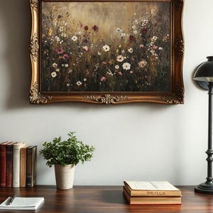 Puede incluir: Una pintura enmarcada de un campo de flores silvestres en tonos de rosa, blanco y morado. La pintura est&aacute; en un marco dorado con detalles ornamentados. La pintura est&aacute; colgada en una pared blanca sobre un escritorio de madera con libros y una planta en maceta.