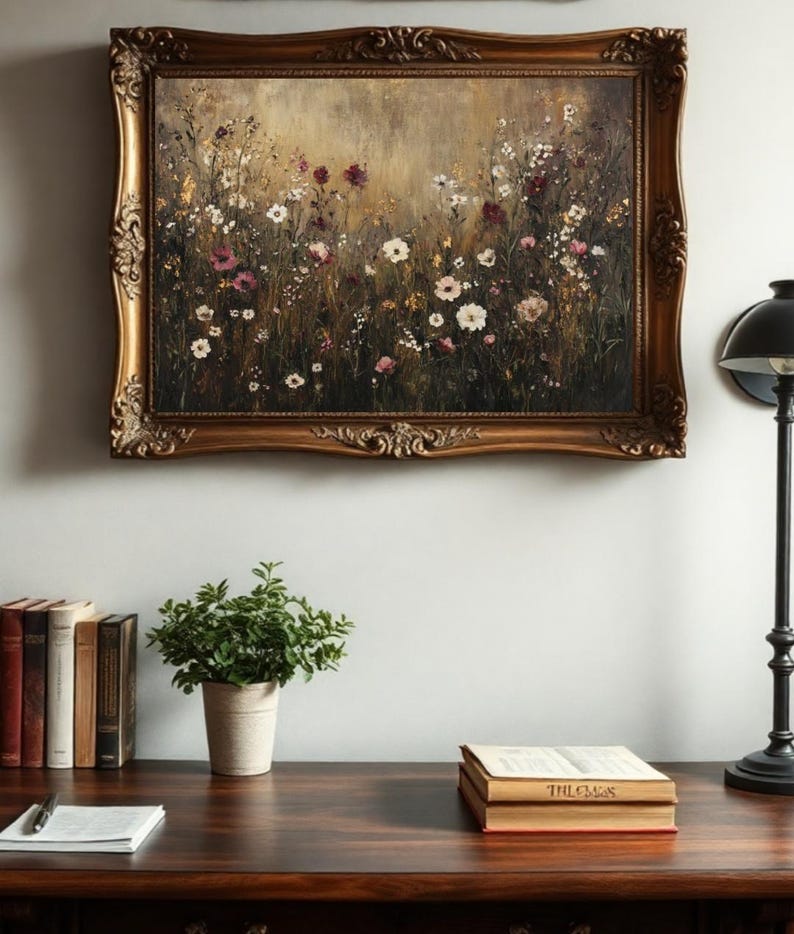 Puede incluir: Una pintura enmarcada de un campo de flores silvestres en tonos de rosa, blanco y morado. La pintura est&aacute; en un marco dorado con detalles ornamentados. La pintura est&aacute; colgada en una pared blanca sobre un escritorio de madera con libros y una planta en maceta.
