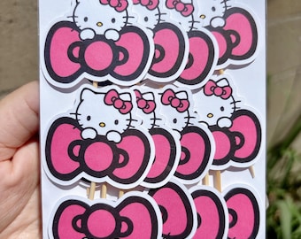 May include: A package of Hello Kitty cupcake toppers. Each topper features a white cat with a pink bow and a large pink bow. The toppers are attached to wooden sticks.