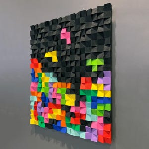 Pode incluir: Uma peça de arte de parede de madeira preta com um design geométrico. A peça é composta por pequenos quadrados de madeira, cada um pintado de uma cor diferente. As cores incluem vermelho, laranja, amarelo, verde, azul, roxo e rosa.