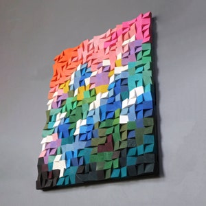 Può includere: Un'opera d'arte murale astratta colorata realizzata in legno. L'opera è composta da molte piccole forme geometriche in tonalità di rosa, rosso, arancio, giallo, verde, blu e viola.