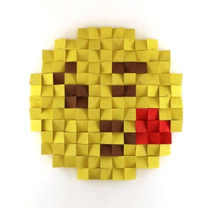 Puede incluir: Una cara sonriente amarilla hecha de bloques de madera. Los ojos son marrones, la boca es roja y la cara está delineada en amarillo.