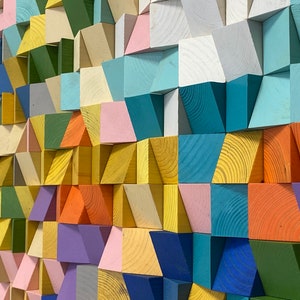Op de afbeelding: Een wandkunstwerk gemaakt van kleurrijke houten blokken die in een geometrisch patroon zijn gerangschikt. De blokken zijn geschilderd in tinten blauw, groen, geel, oranje, roze en paars.