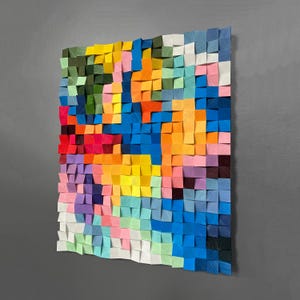May include: A colourful abstract wall art piece made of wooden blocks. The blocks are arranged in a grid pattern and are painted in various shades of blue, green, yellow, orange, red, and pink.